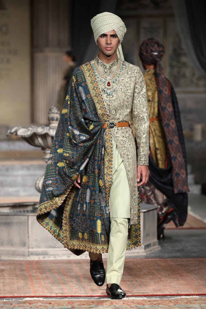 creative-01 Male model in ornate traditional outfit walking runway at fashion show.