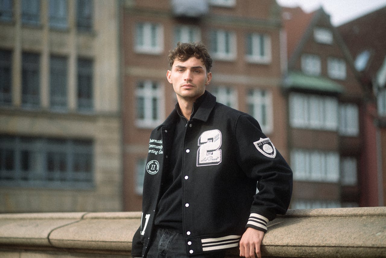 creative-02 Young man in a stylish baseball jacket posing in a cityscape.