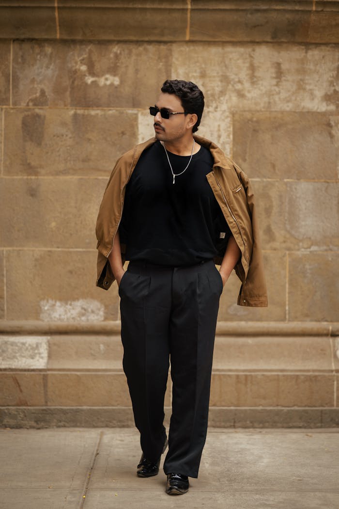 Stylish man walking in a city, wearing sunglasses and casual attire.