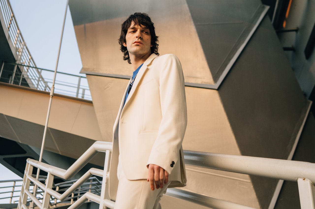 brand-01 Portrait of a stylish man in a beige suit with architectural backdrop, capturing modern fashion elegance.